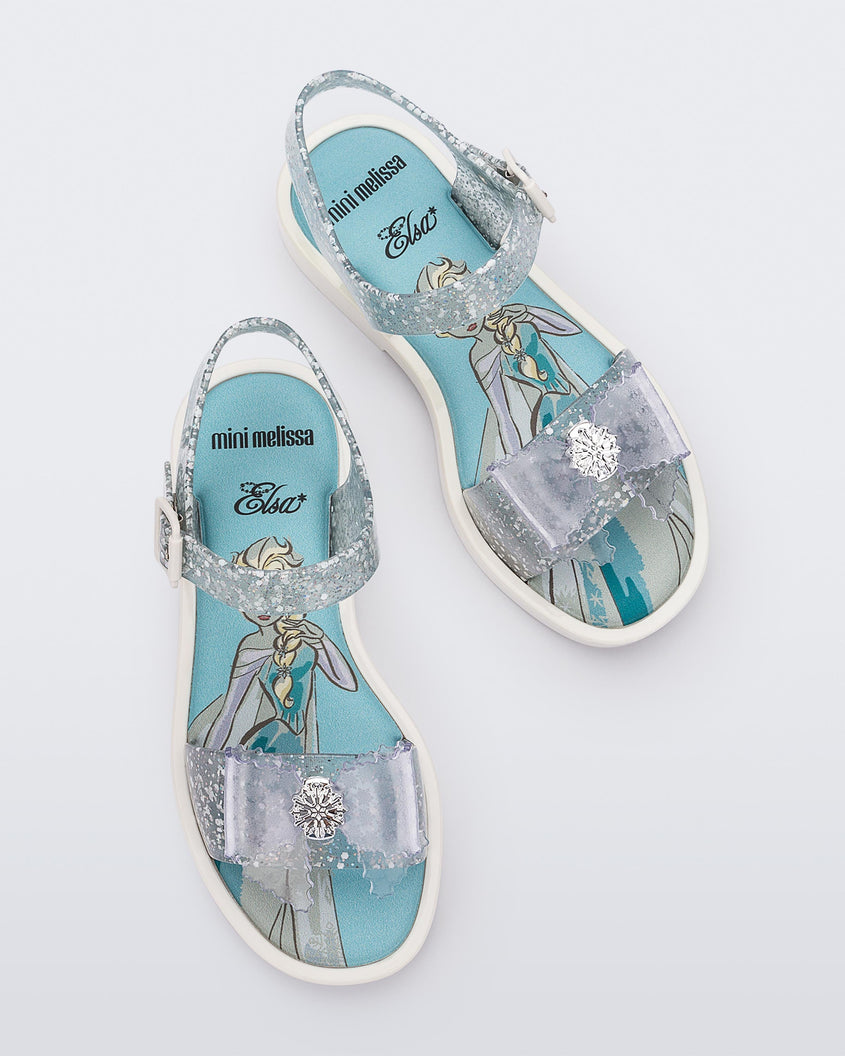 Top view of a pair of glitter clear Mini Melissa Mar Sandal Princess sandals with a snowflake bow detail on the front strap, an ankle strap and Princess Elsa soul