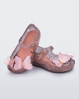Angled view of a pair of clear/glitter pink Ultragirl Butterfly baby ballerina flats with pink butterflies