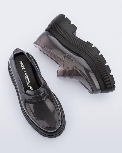 Top and side view of a pair of transparent smoke Royal High + Undercover platform loafers with black sole. 