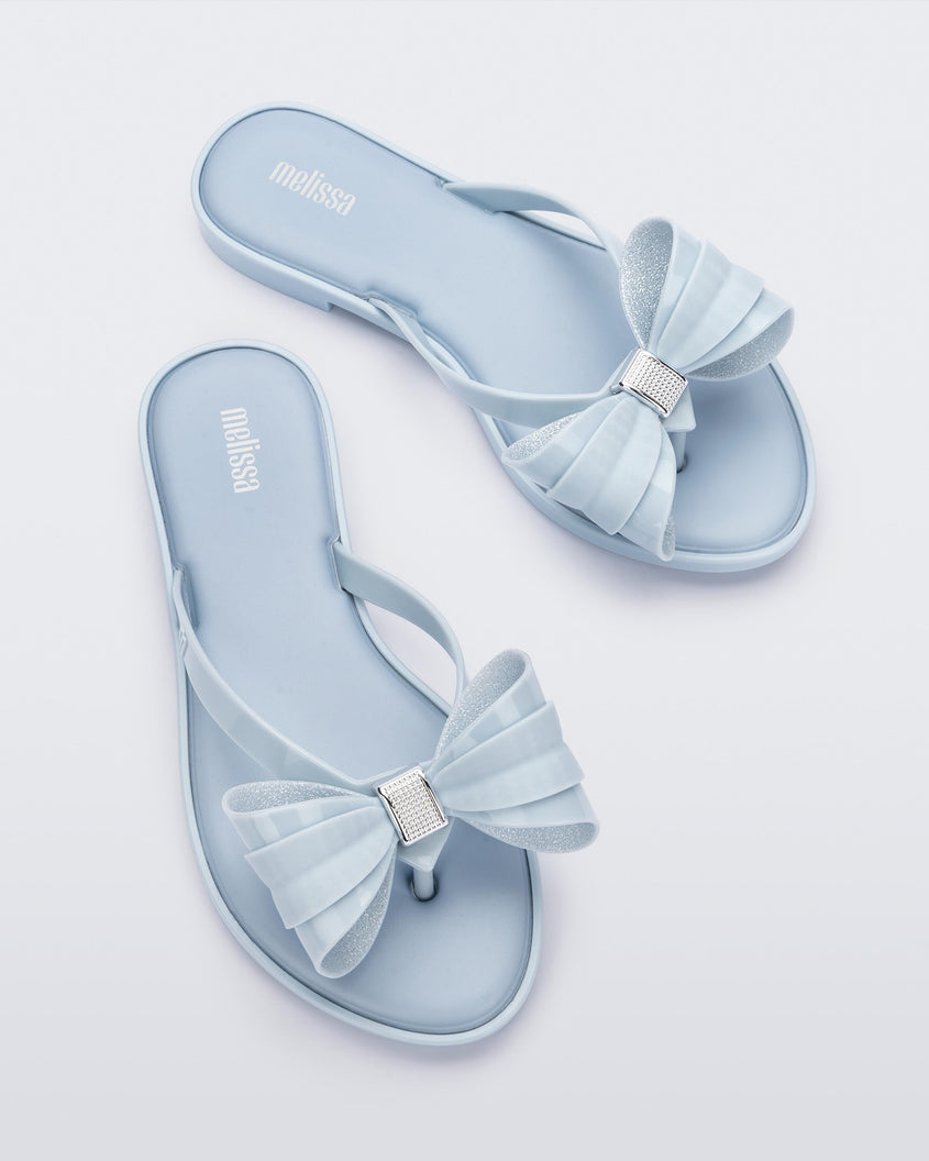 Overhead view of a pair of Melissa slim strap flip flops in glitter blue with bow applique