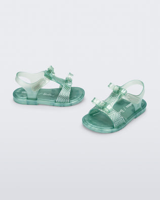 Side and angled view of a pair of pearly green baby Dream Sandal with two bows and gold detail on strap