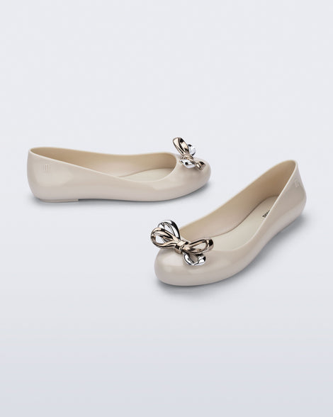Side and angled view of a pair of beige Sweet Love Glam ballerina flats with chrome bow