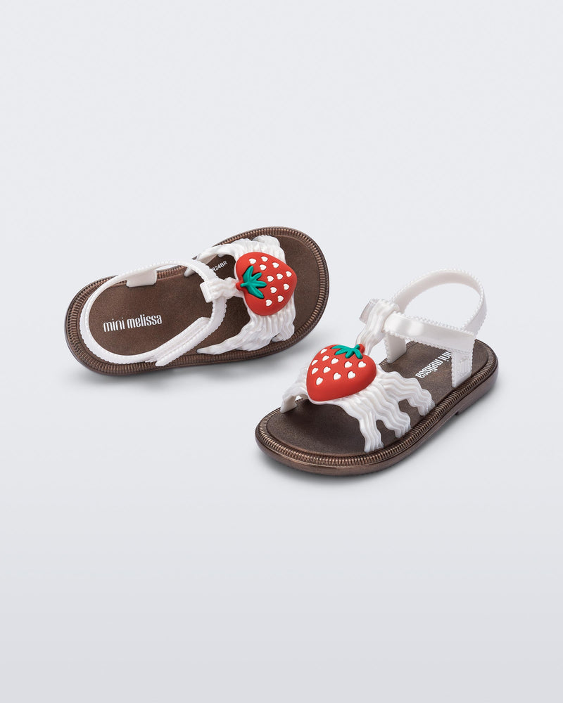 Angled view of a pair of pearly white baby Hip Sandals with red strawberry