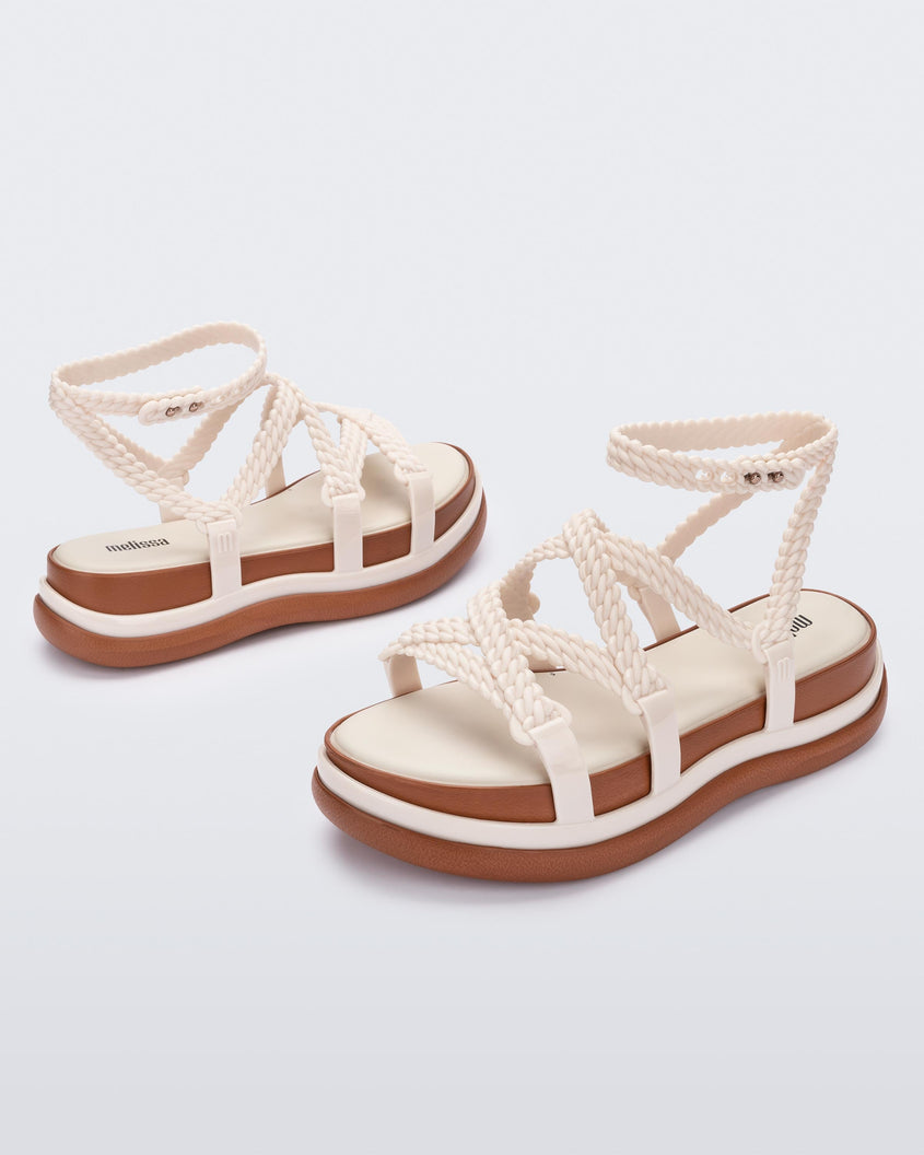 An angled front and side view of a pair of beige Melissa Buzios platform sandals with multiple textured straps that mimic sisal braids across the front of the shoe as well as an ankle strap