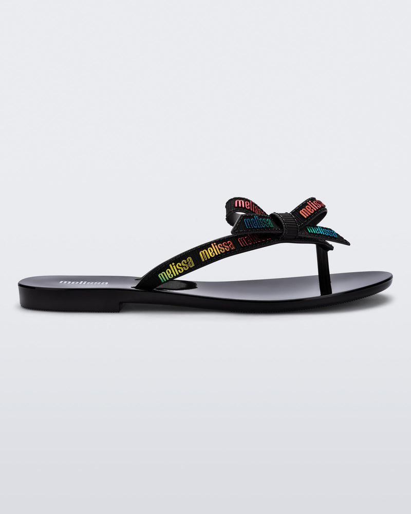 Side view of a black Harmonic M Lover adult flip flop with rainbow Melissa logo on strap
