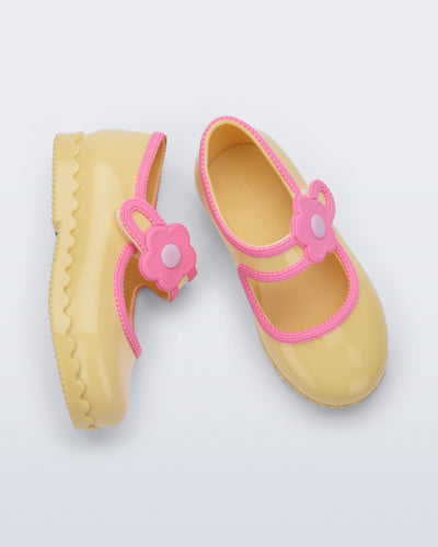Side and top  view of a pair of yellow Hip Ballerina baby flats with flower on strap and pink trim
