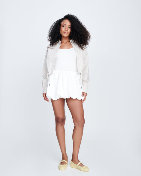 Model in a white skirt and top wearing a pair of yellow Soft Ballerina Delicate Bow flats with top strap and bow