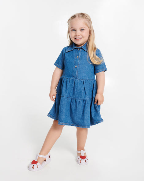 Child model in a blue dress wearing a pair of white Hip Heart Ballerina baby sandals with red heart on front