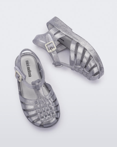 Top and side view of a pair of Mini Melissa Possession baby sandals in glitter clear with velcro buckle closure on the ankle straps