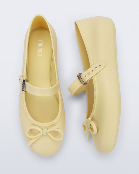 Side and top view of a pair of yellow Soft Ballerina Delicate Bow flats with top strap and bow