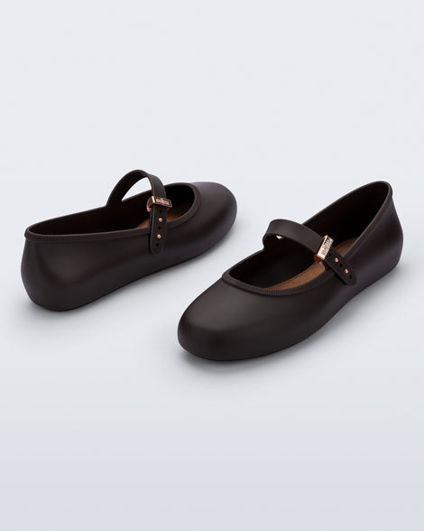 Back and angled view of a pair of brown Soft Ballerina flats with top strap and rose gold buckle