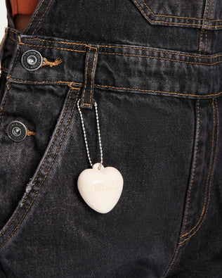 Close up view of a woman's overalls with a beige Heart Charm attached to the belt loop