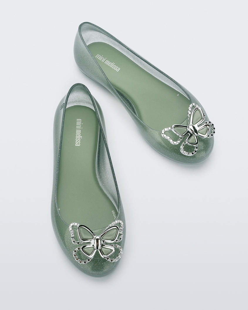 Top view of a pair of glitter green Mini Melissa Sweet Love Butterfly flats with a silver butterfly detail on the toe