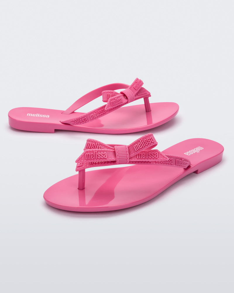 Angled view of a pair of pink Harmonic M Lover adult flip flop with Melissa logo on strap