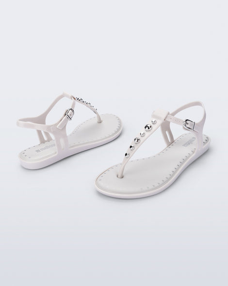 Angled view of a pair of white Solar Boho t-strap sandals with ,metallic detailing on the front strap