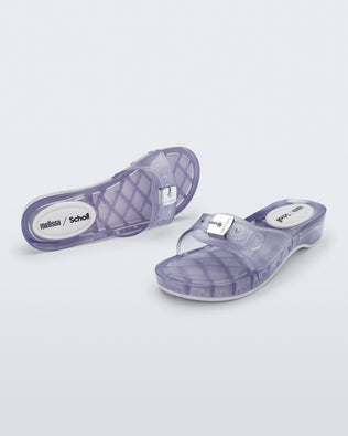 Top and angled view of a pair of clear Pescura Heel + Scholl slides with top buckle