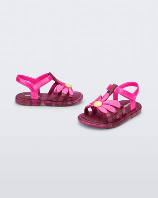 Angled view of a pair of glitter pink baby Hip Bloomy sandal with pink straps and flower