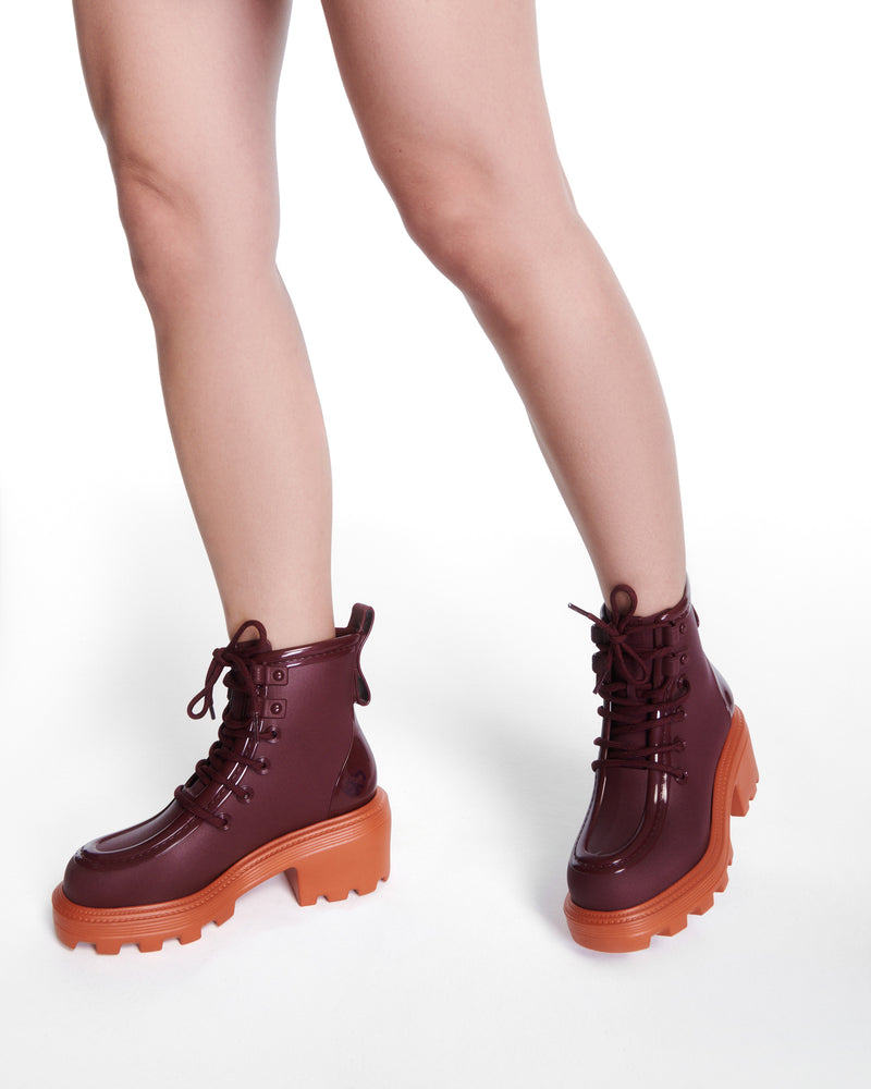 Model's legs wearing a pair of burgundy Track Boot with small heel and burgundy laces and orange sole