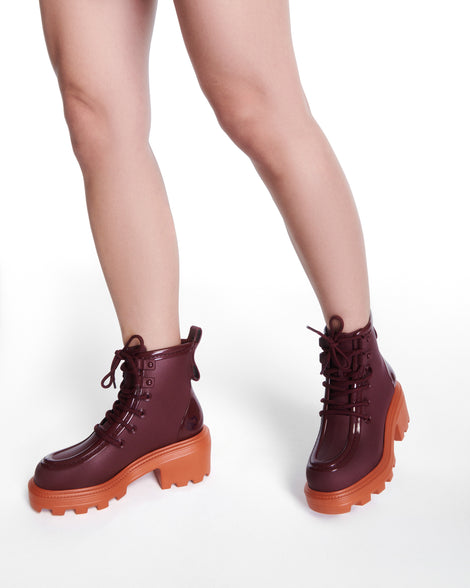 Model's legs wearing a pair of burgundy Track Boot with small heel and burgundy laces and orange sole
