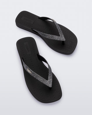 Top view of a pair of black with silver strap Sun Long Beach flip flop