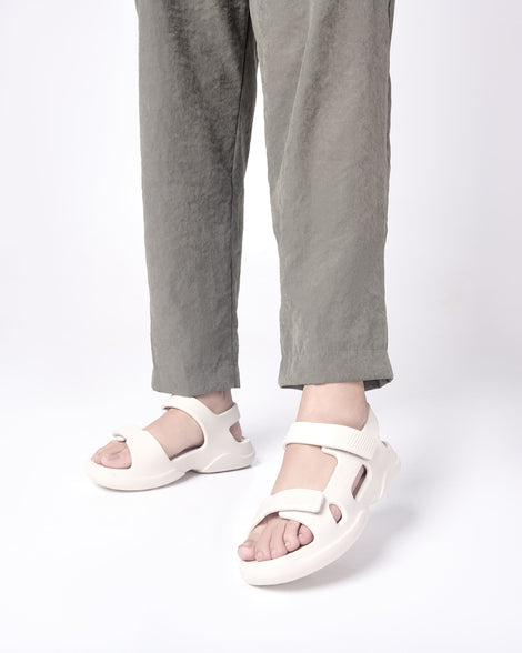 Model's legs in grey pants wearing a pair of beige Free Papete sandals.