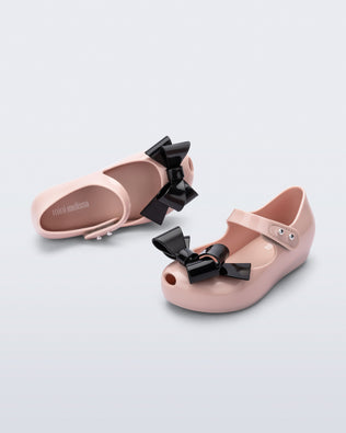 Top and side angled view of a pair of pink Ultragirl Classy baby ballerina flats with black bow