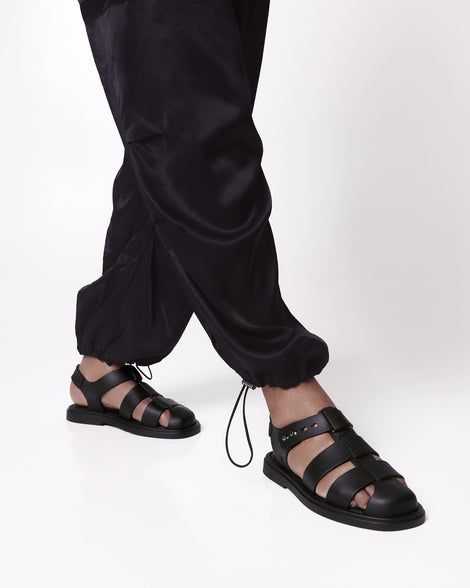 Model's legs in black pants wearing a pair of black Emma women's sandals.