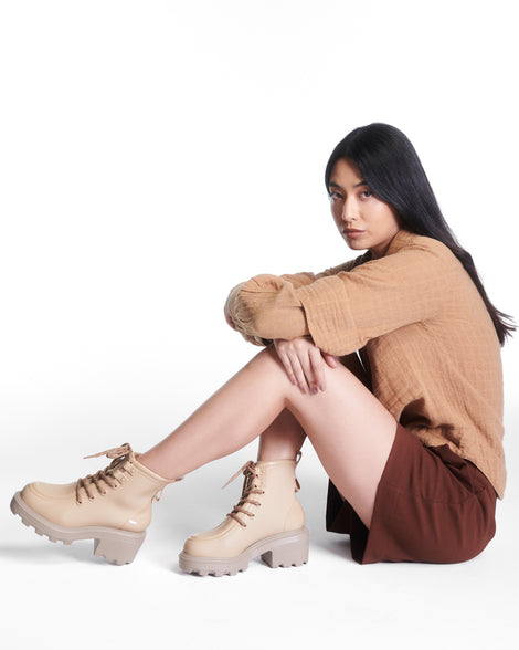 Model sitting down in a brown outfit wearing a pair of beige Track Boot with small heel and beige laces