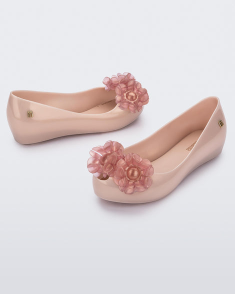 Angled view of a pearly pink Ultragirl Springtime kids flat with two clear pink flowers and peep toe.