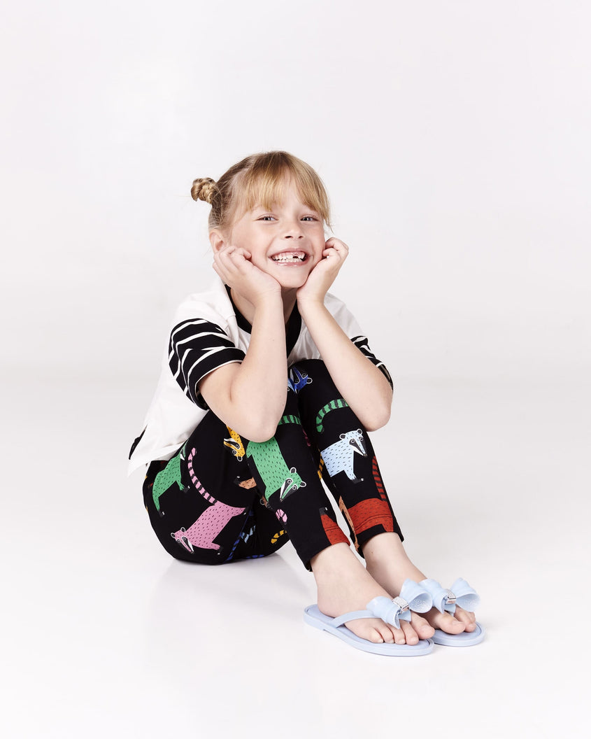 Model siting and posing wearing a pair of Mini Melissa Flip Flops in blue with bow applique