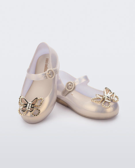 An angled front and top view of a pair of pearly gold Mini Melissa Sweet Love Butterfly flats, leaning on eachother, with a top strap and a gold butterfly detail on the toe