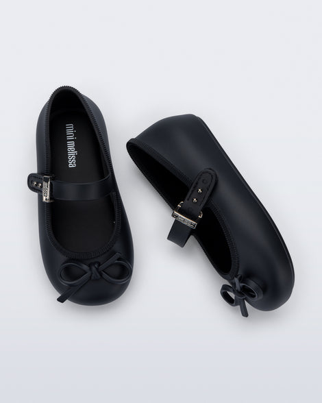Side and top view of a pair of black Soft Ballerina Delicate Bow baby flats with top strap and bow
