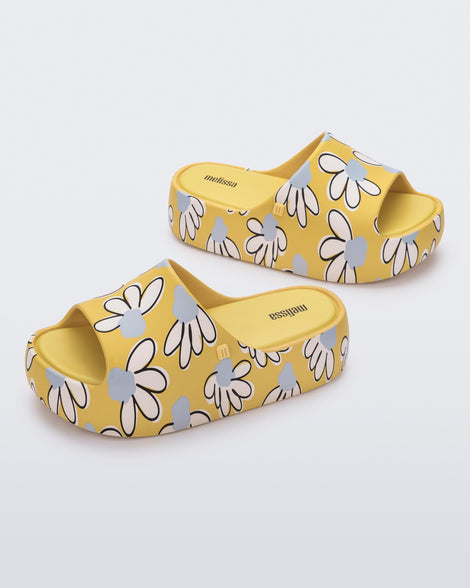 Angled view of a pair of yellow Free Print Platform slides with a white and blue flower print.