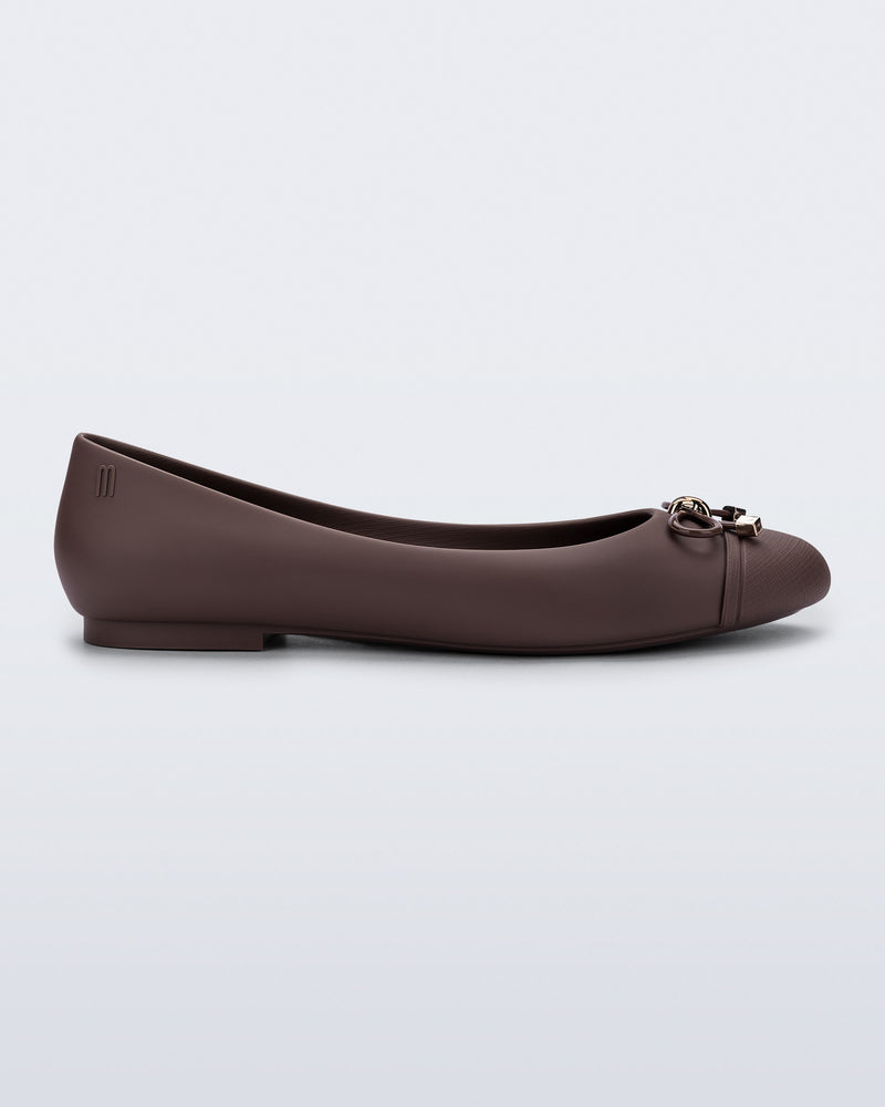 Side view of a brown Melissa flat with bow detail with gold accents on the bow