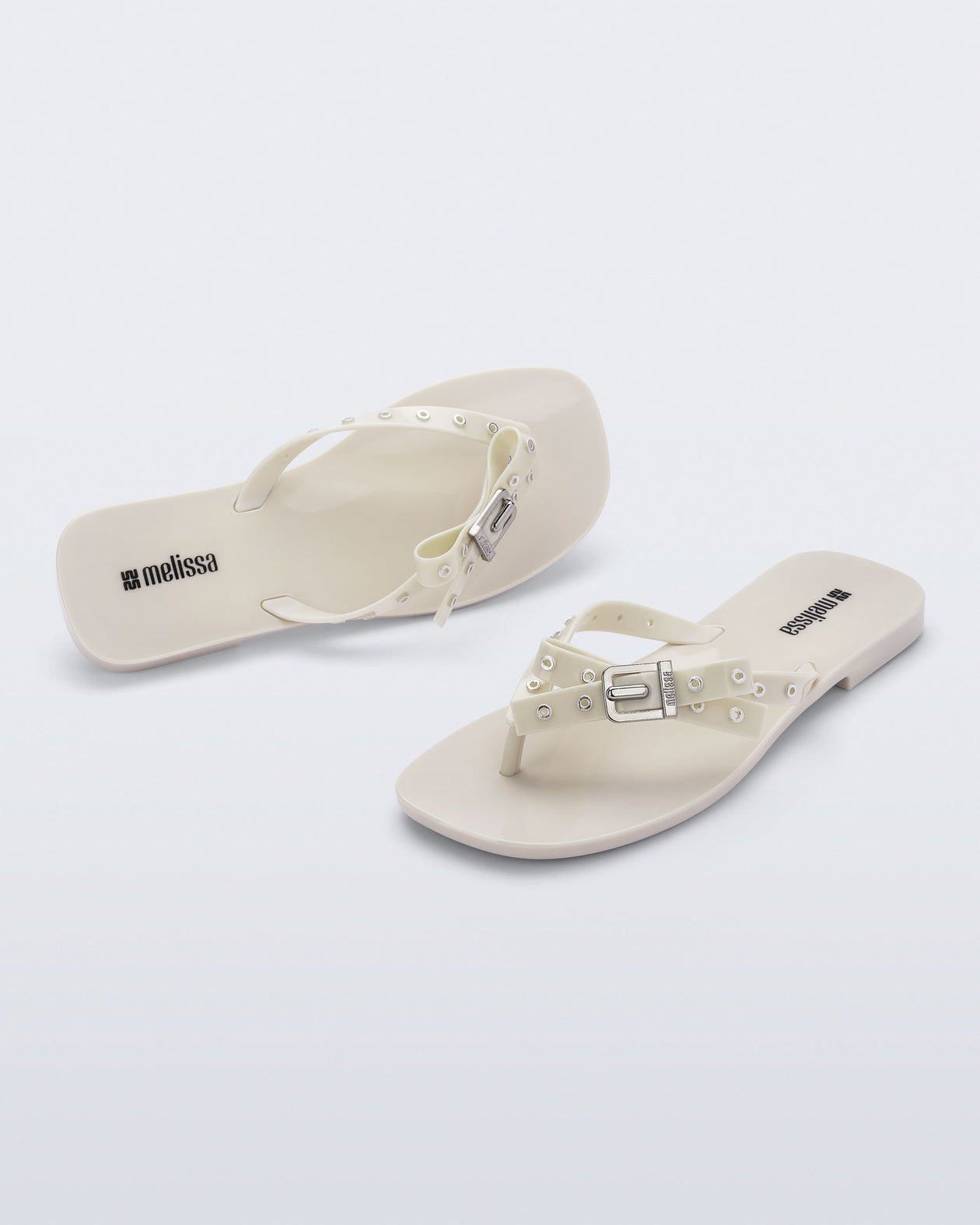 Side and angled view of a pair of beige Harmonic Squared flip flops with bow on strap