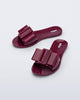 Angled view a pair of burgundy Babe slide sandals with large bow on top.
