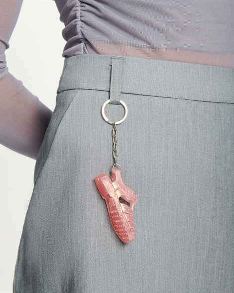 Close up view of a woman's grey skirt with a glitter pink Possession keychain attached to the belt loop