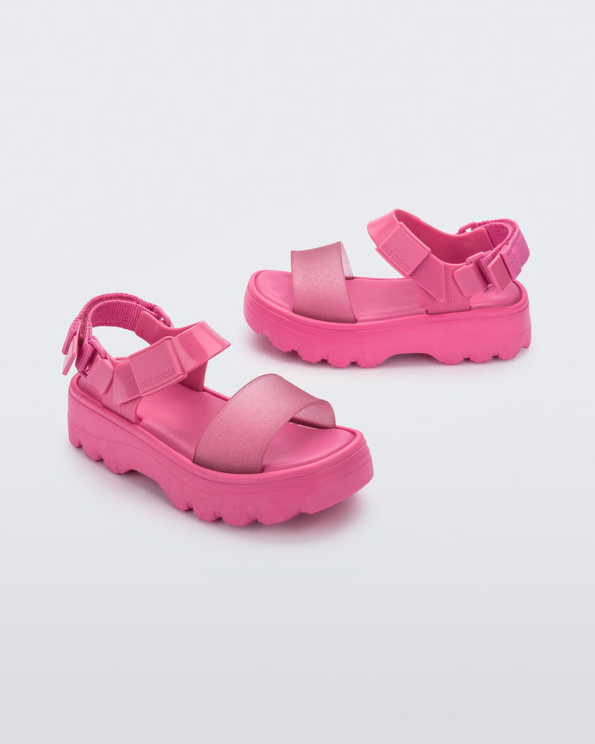 Angled view of a pair of Mini Melissa Kick Off platform sandals in pink with adjustable velcro ankle straps 