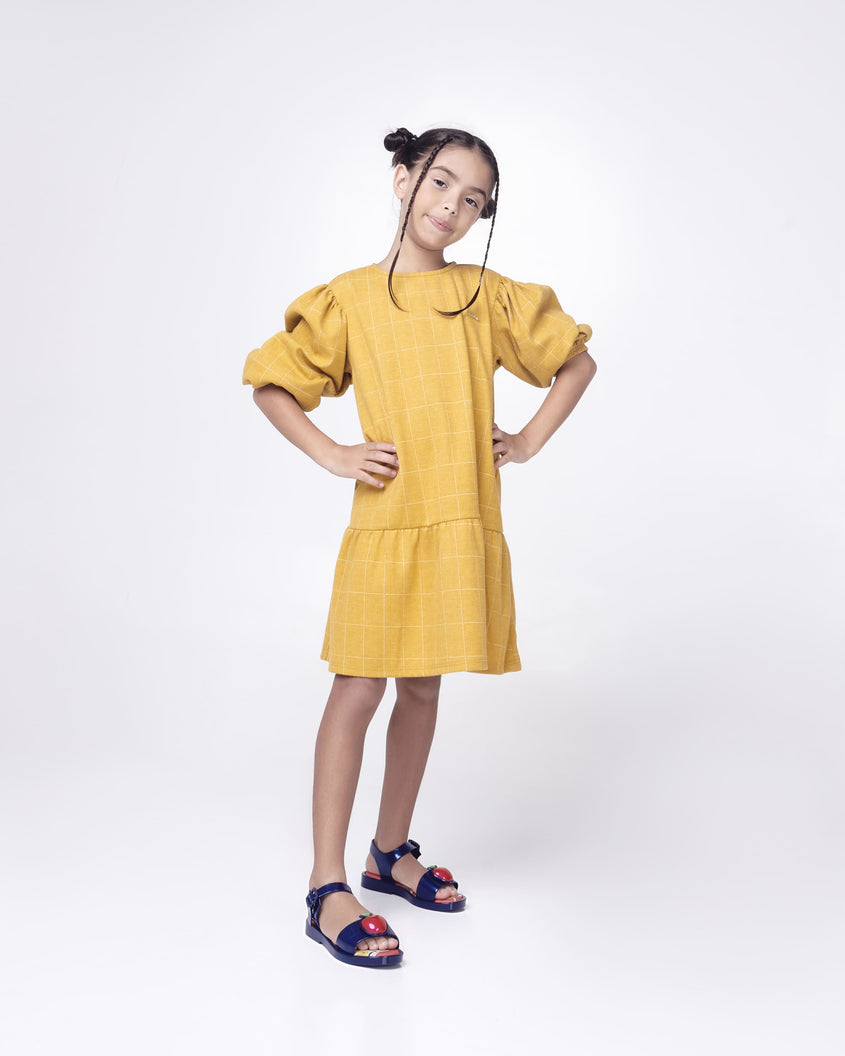 A kid model posing for a picture in a yellow dress and a pair of metallic blue Mini Melissa Mar Sandal Princess sandals with an apple detail on the front strap, an ankle strap and Princess Snow White soul