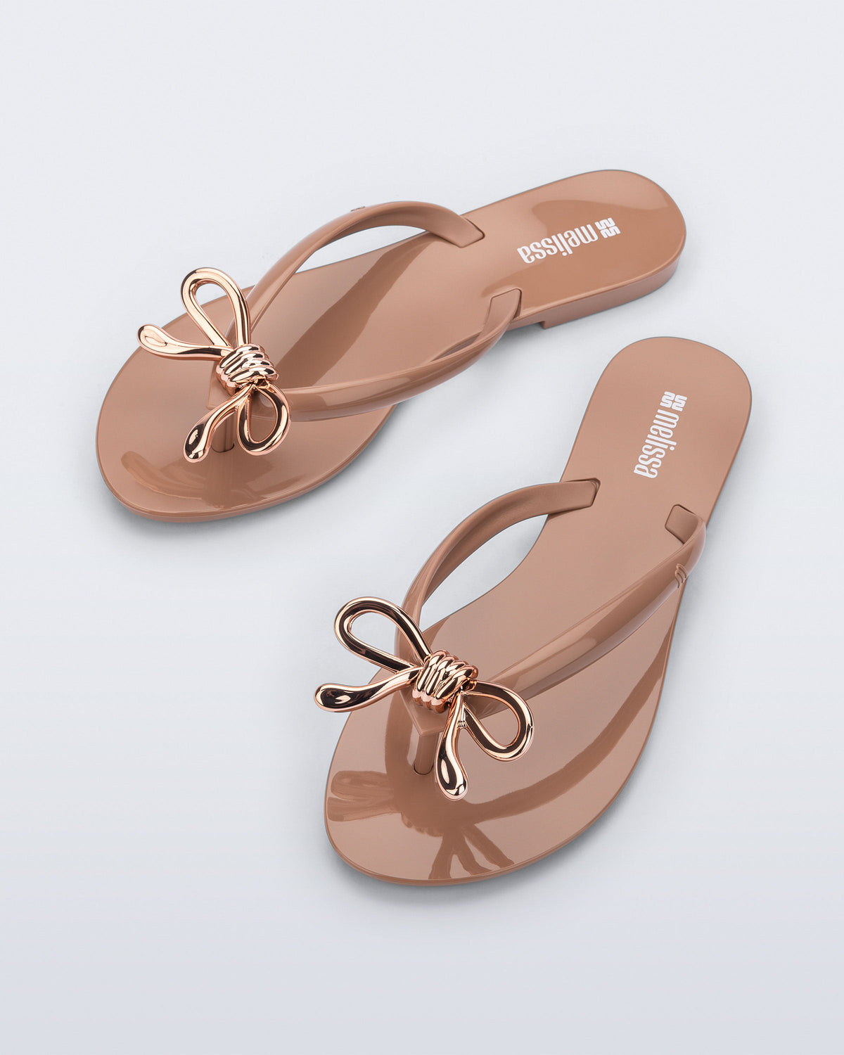 Top view of a pair of brown Harmonic Iris flip flops with rose gold bow