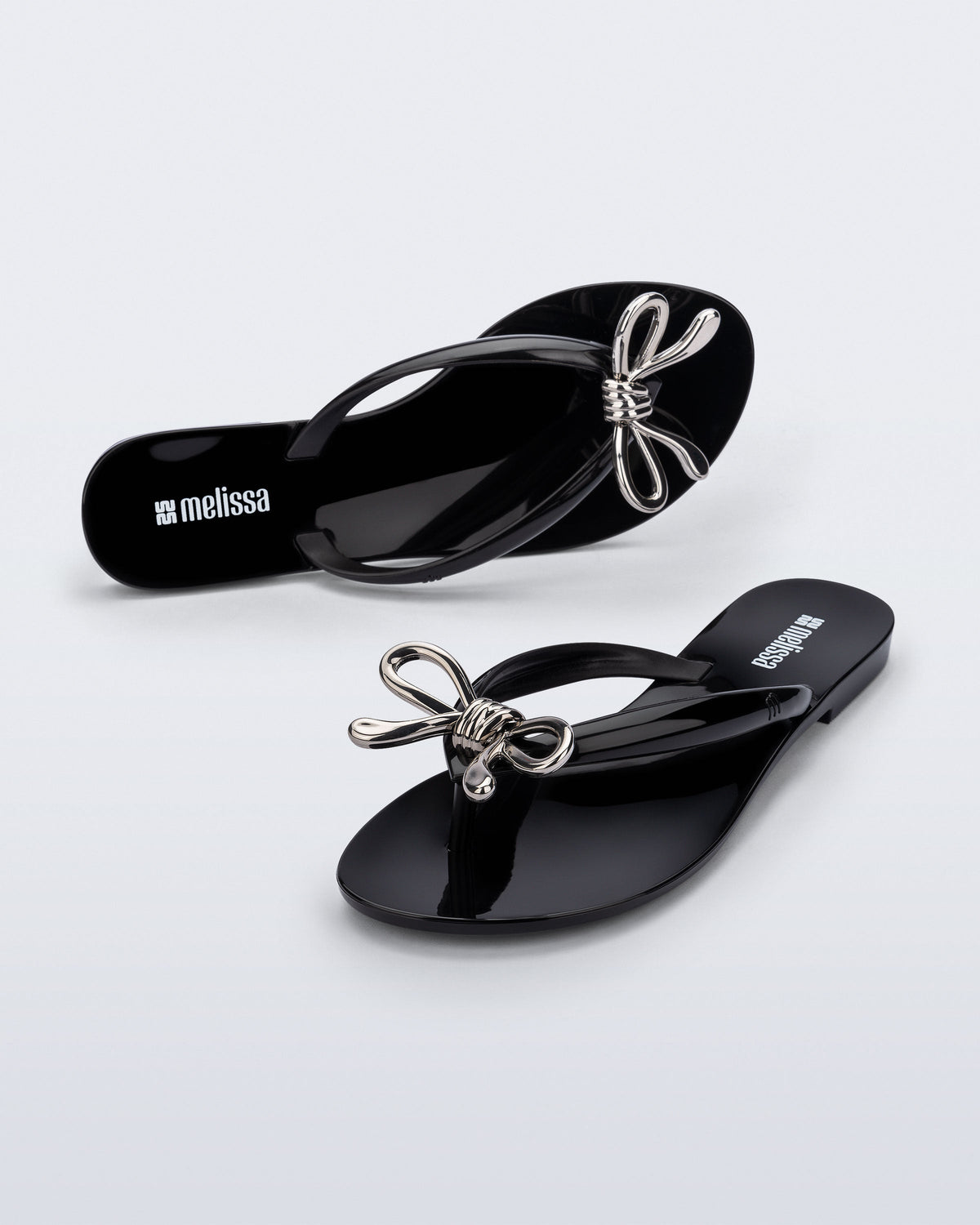 Top and angled view of a pair of black Harmonic Iris flip flops with silver bow