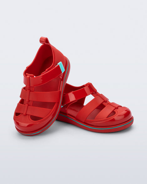 Angled view of a pair of red Smash closed toe baby sandals with blue trim