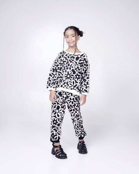 Child model in a black and white patterned outfit wearing a pair of black Megan kids heel sandals.
