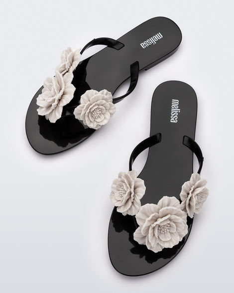 Top view of a pair of a black Harmonic Springtime women's flip flop with 3 beige flowers