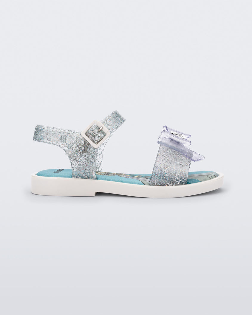 Side view of a glitter clear Mini Melissa Mar Sandal Princess sandal with a snowflake bow detail on the front strap, an ankle strap and Princess Elsa soul