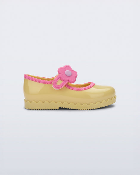 Side view of a yellow Hip Ballerina baby flat with flower on strap and pink trim