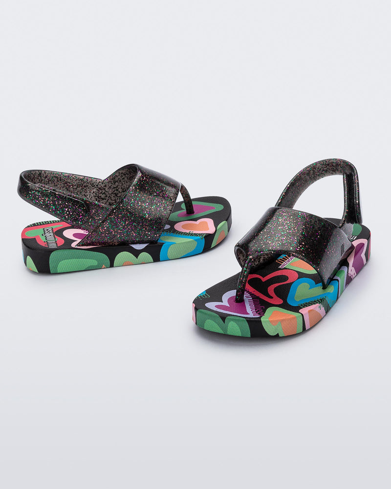 Angled view of a pair of black glitter Shiny baby sandals with multicolor sole