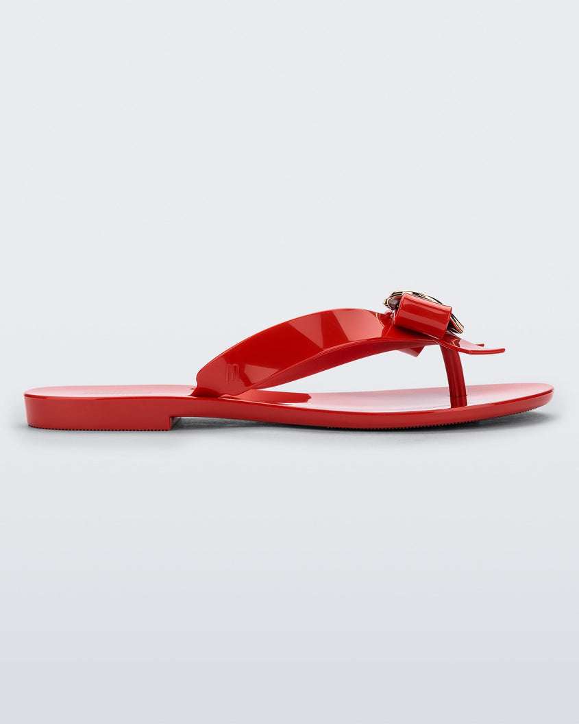 Side view of a red Melissa Harmonic Heart flip flop with a red bow and gold heart detail on the straps