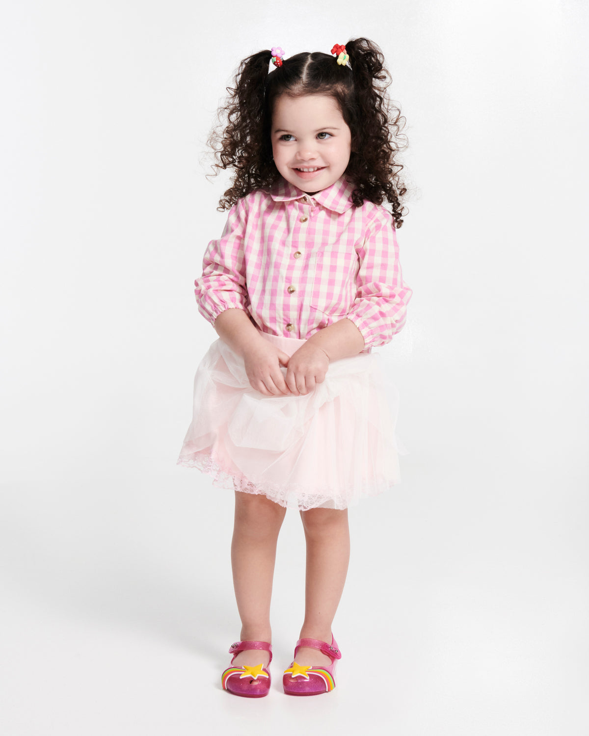 Child model in a pink shirt and skirt wearing a pair of glitter pink Ultragirl Colors baby flats with yellow star and rainbow on top