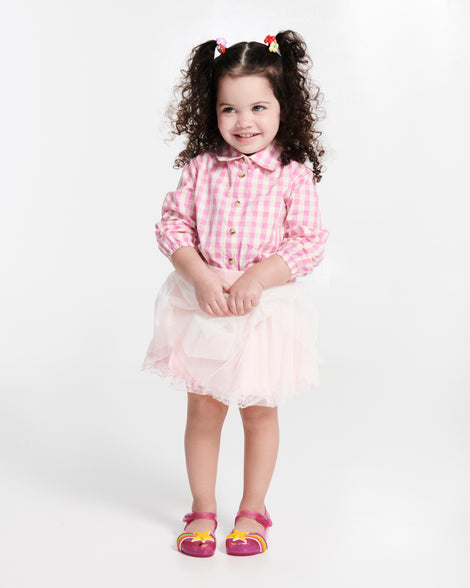 Child model in a pink shirt and skirt wearing a pair of glitter pink Ultragirl Colors baby flats with yellow star and rainbow on top